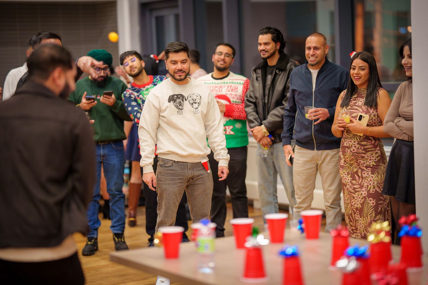 Crowd gathers around display of red plastic cups arranged in formation on hardwood floor.