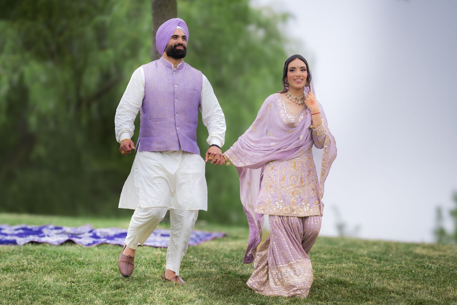 A couple in traditional Indian attire walking together on a grassy hill during their photoshoot.