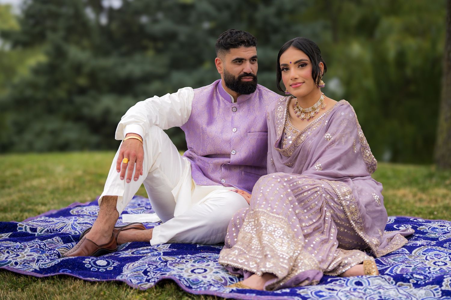 Romantic outdoor portrait session with couple in coordinated lavender outfits on blue patterned blanket.