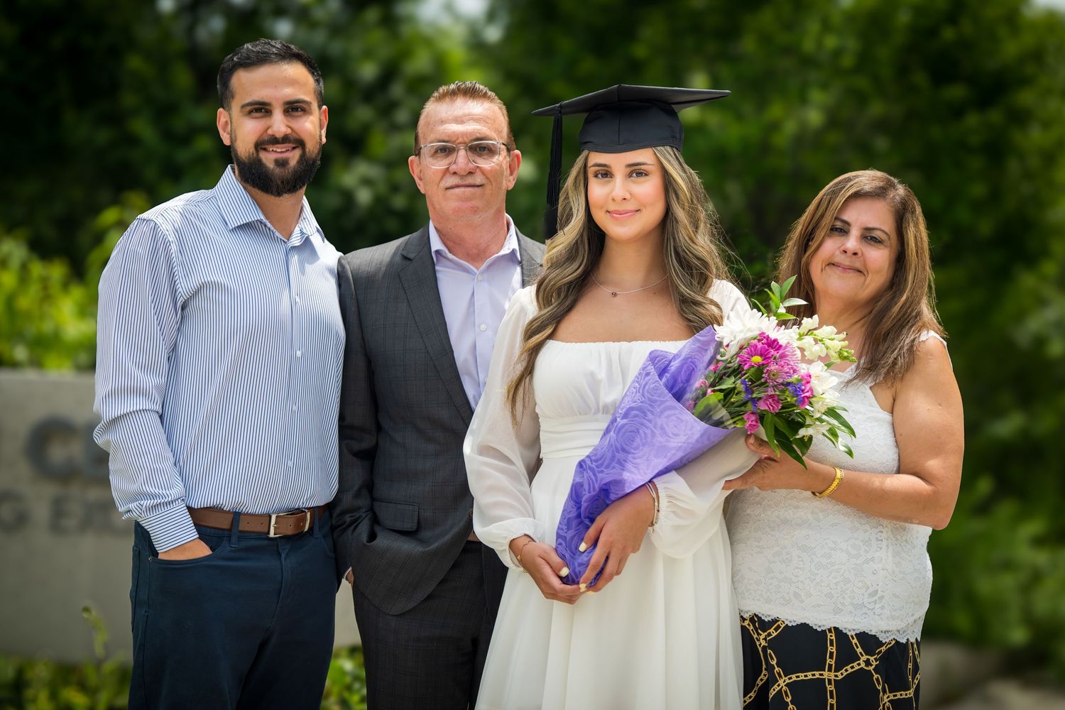 Graduation celebration group photo with purple flowers and white dress.