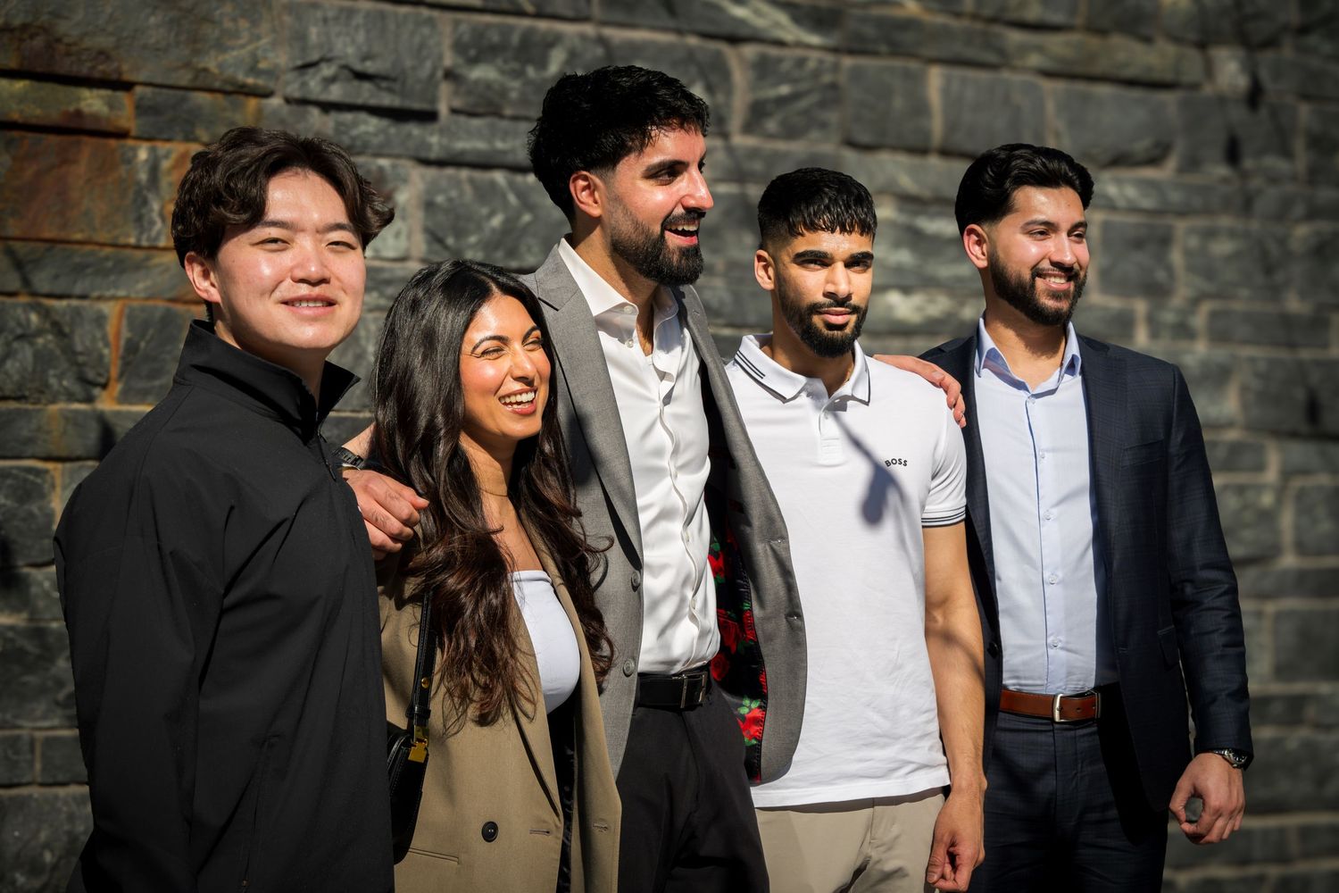 Casual group portrait against an industrial stone wall background.