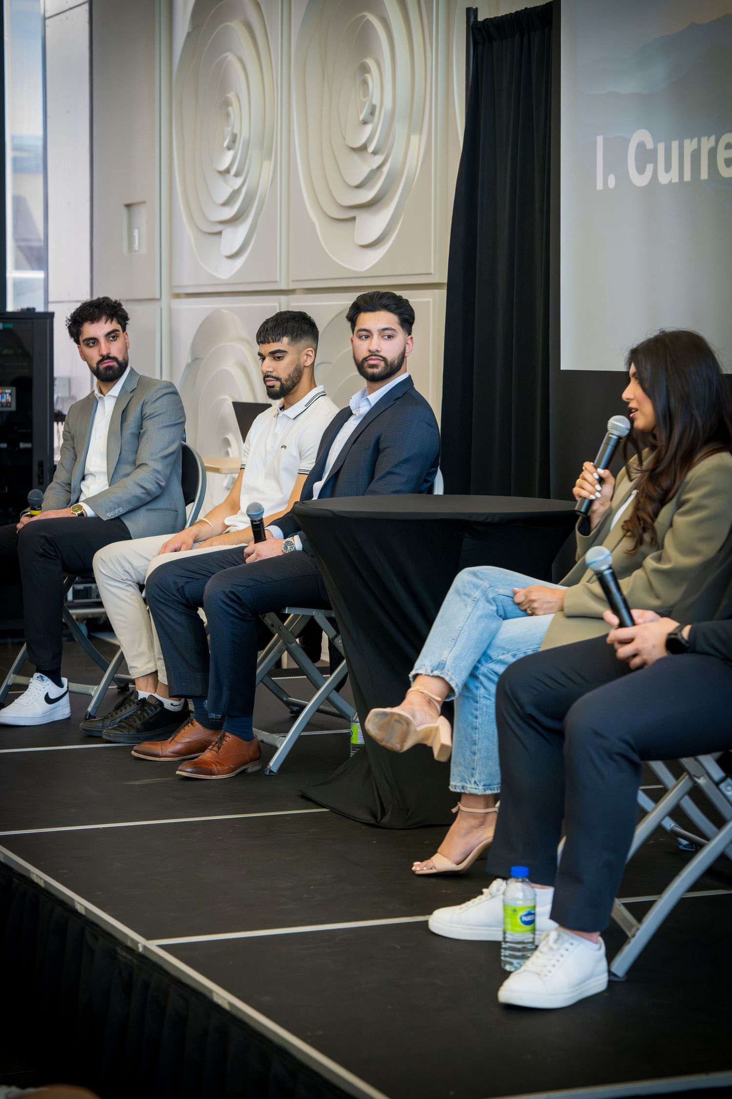Professional panel discussion showing speakers in business attire seated on folding chairs.