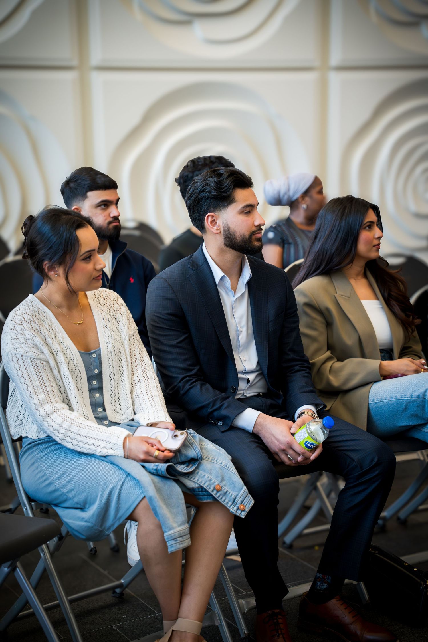 Attendees in business and casual wear seated during indoor presentation event.