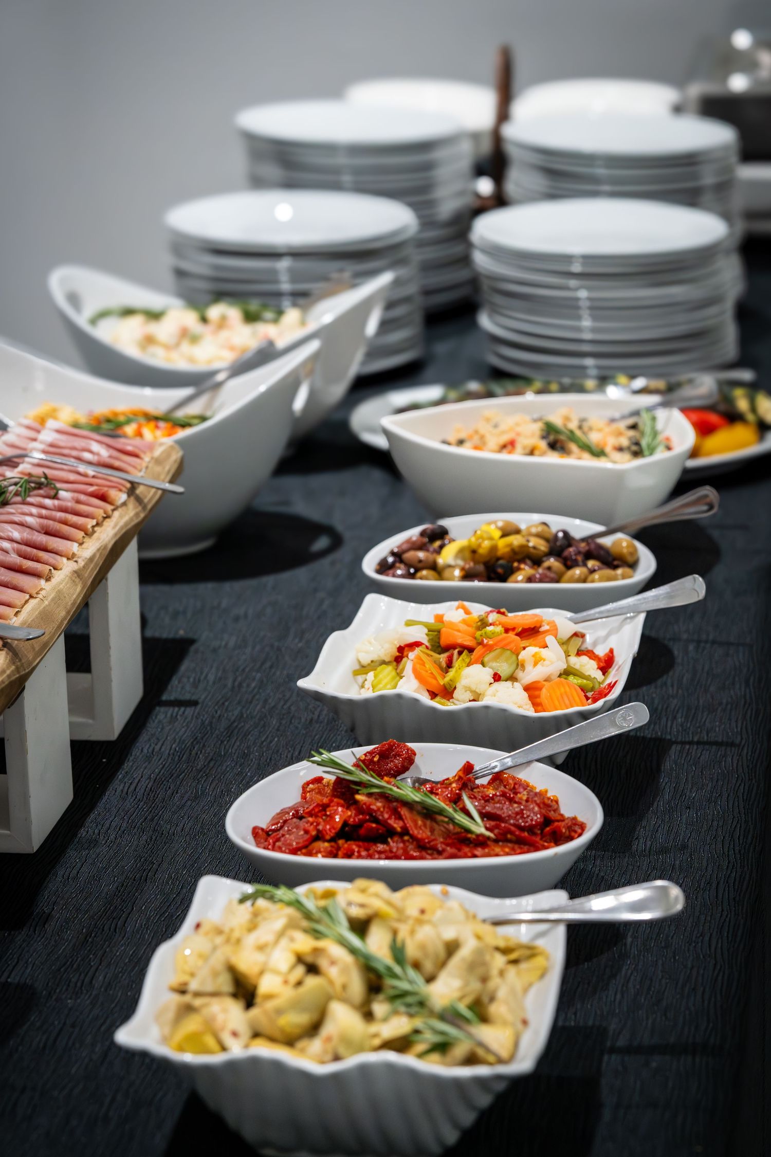 An elegant catering display featuring charcuterie boards and appetizer dishes with stacks of white plates in the background.