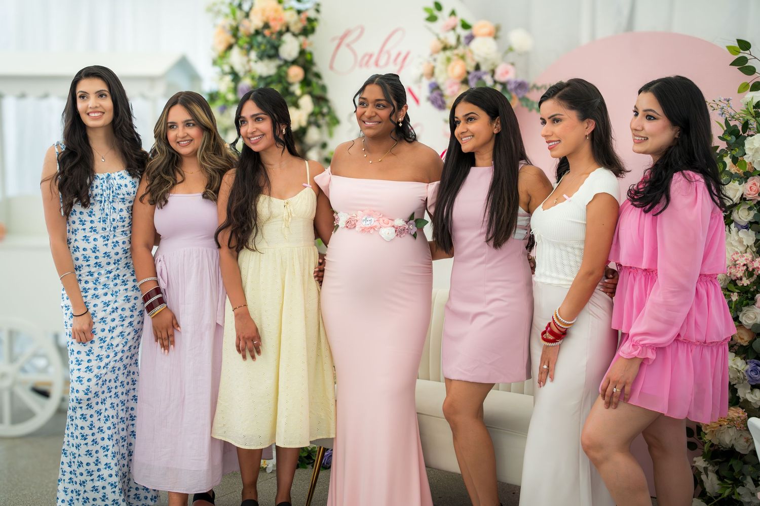 Baby shower celebration with guests wearing coordinated pink and pastel dresses.