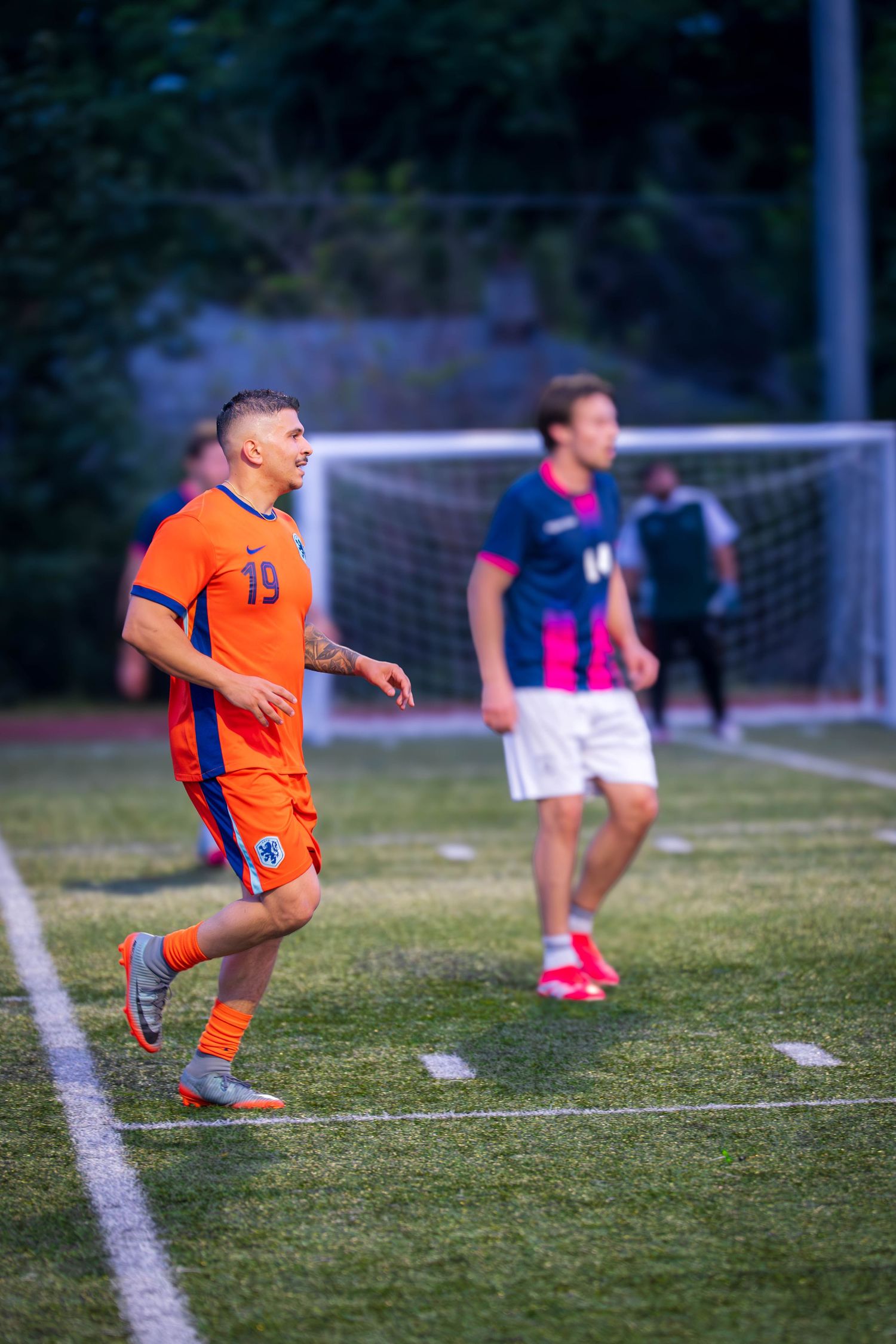 Player in orange uniform number 19 positions during soccer match with goal in background.