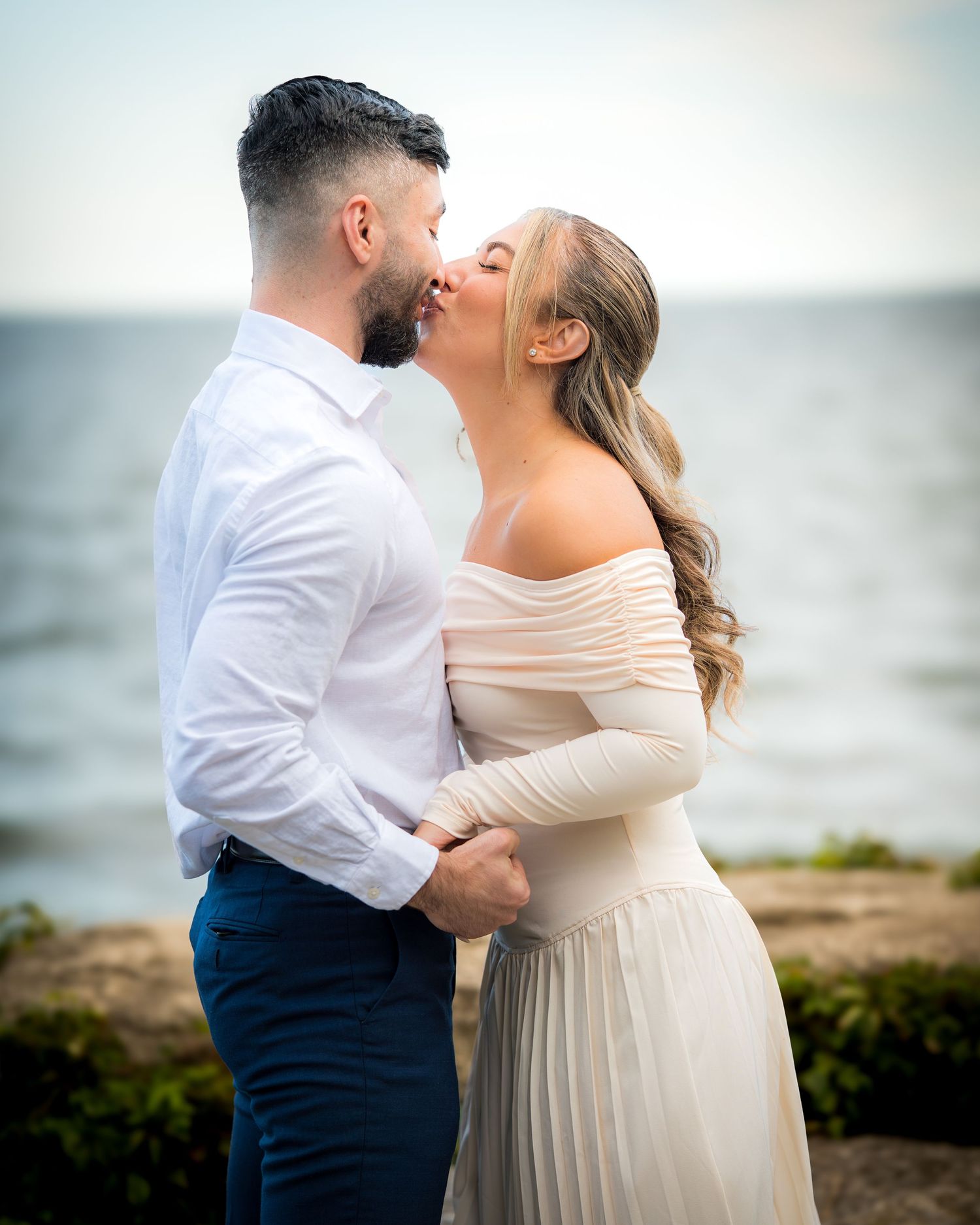 A couple in formal wear shares a romantic moment by the sea.