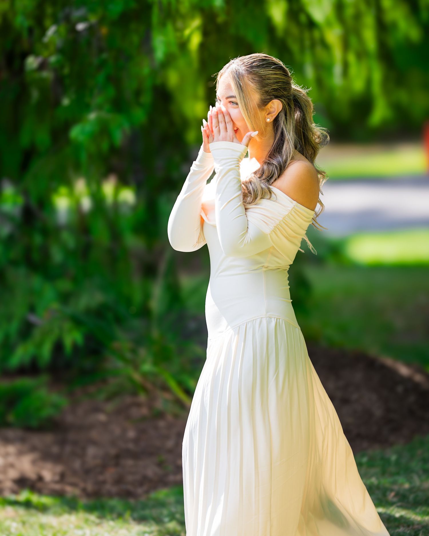 A person in a flowing white dress stands in a garden setting with lush green foliage in the background.