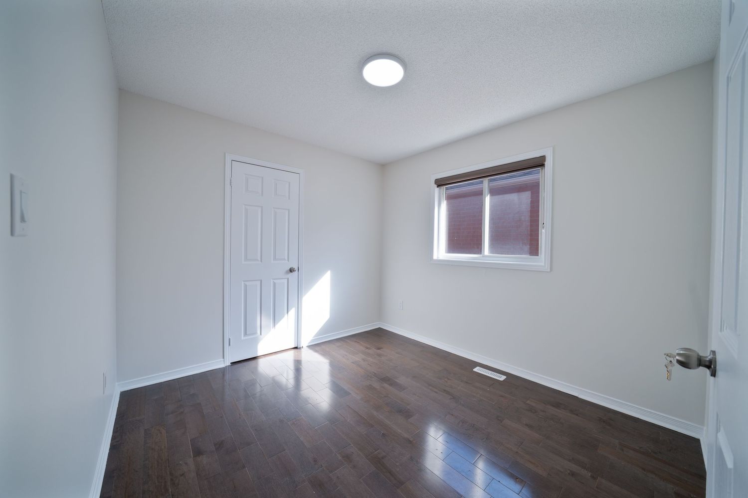 A modern apartment interior showing a hallway with white walls, hardwood floors, and recessed lighting.