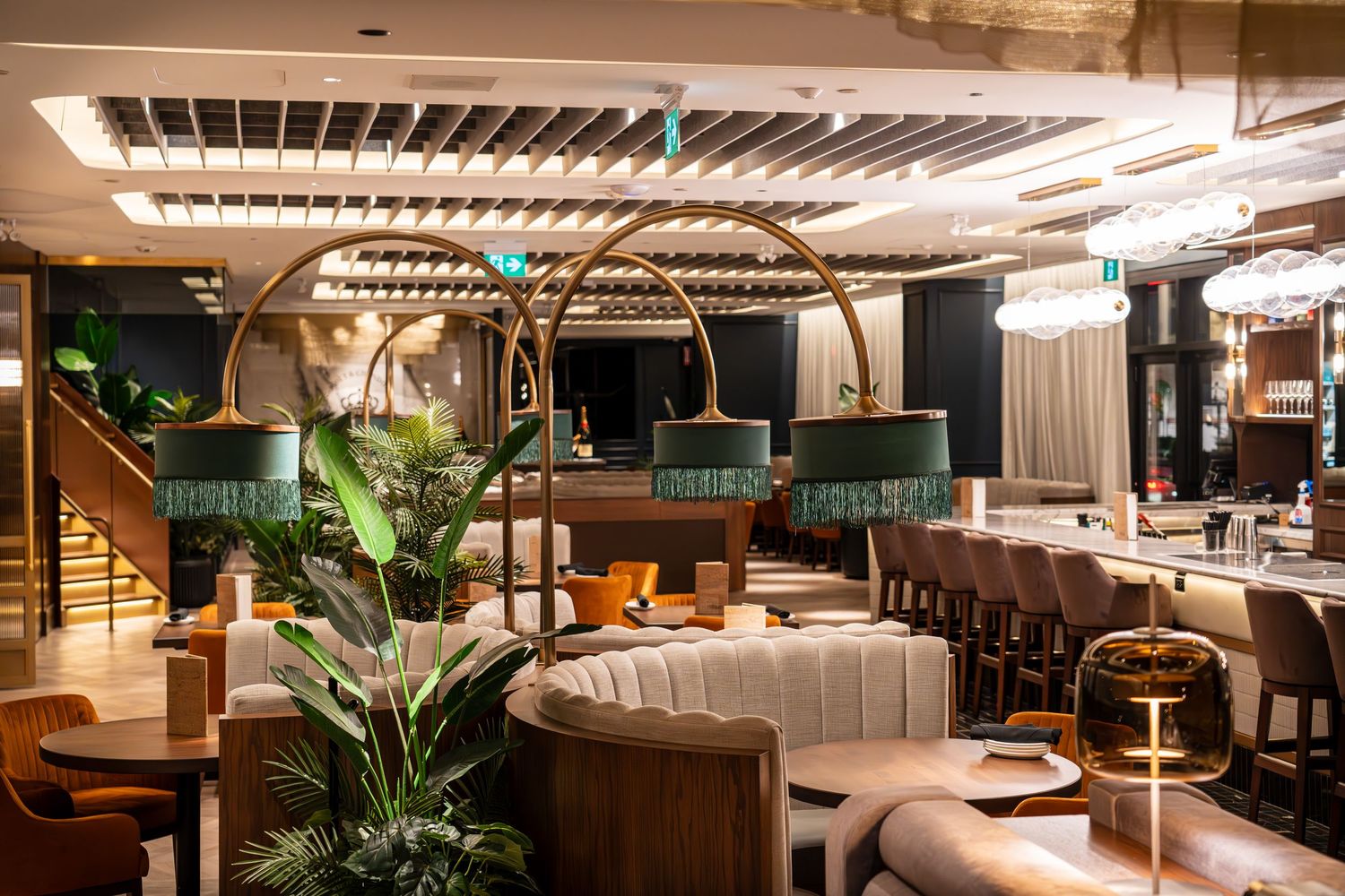Modern restaurant interior with curved booth seating, pendant lighting, and lush green plants creating an elegant atmosphere.