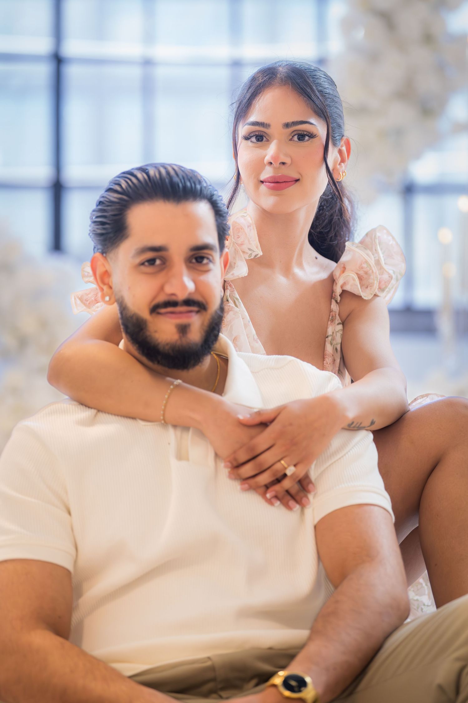 Engaged couple posing together surrounded by white floral decorations after a proposal.