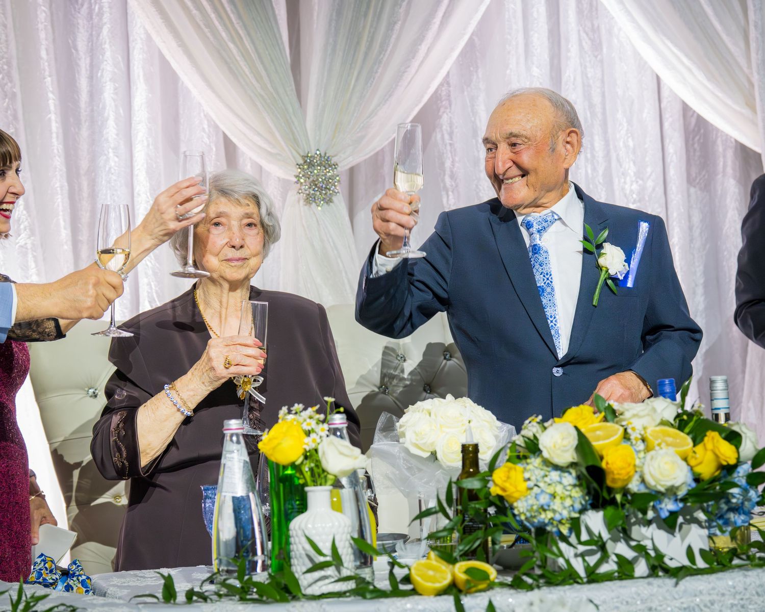Elderly couple raising champagne glasses for a toast at wedding anniversary reception.