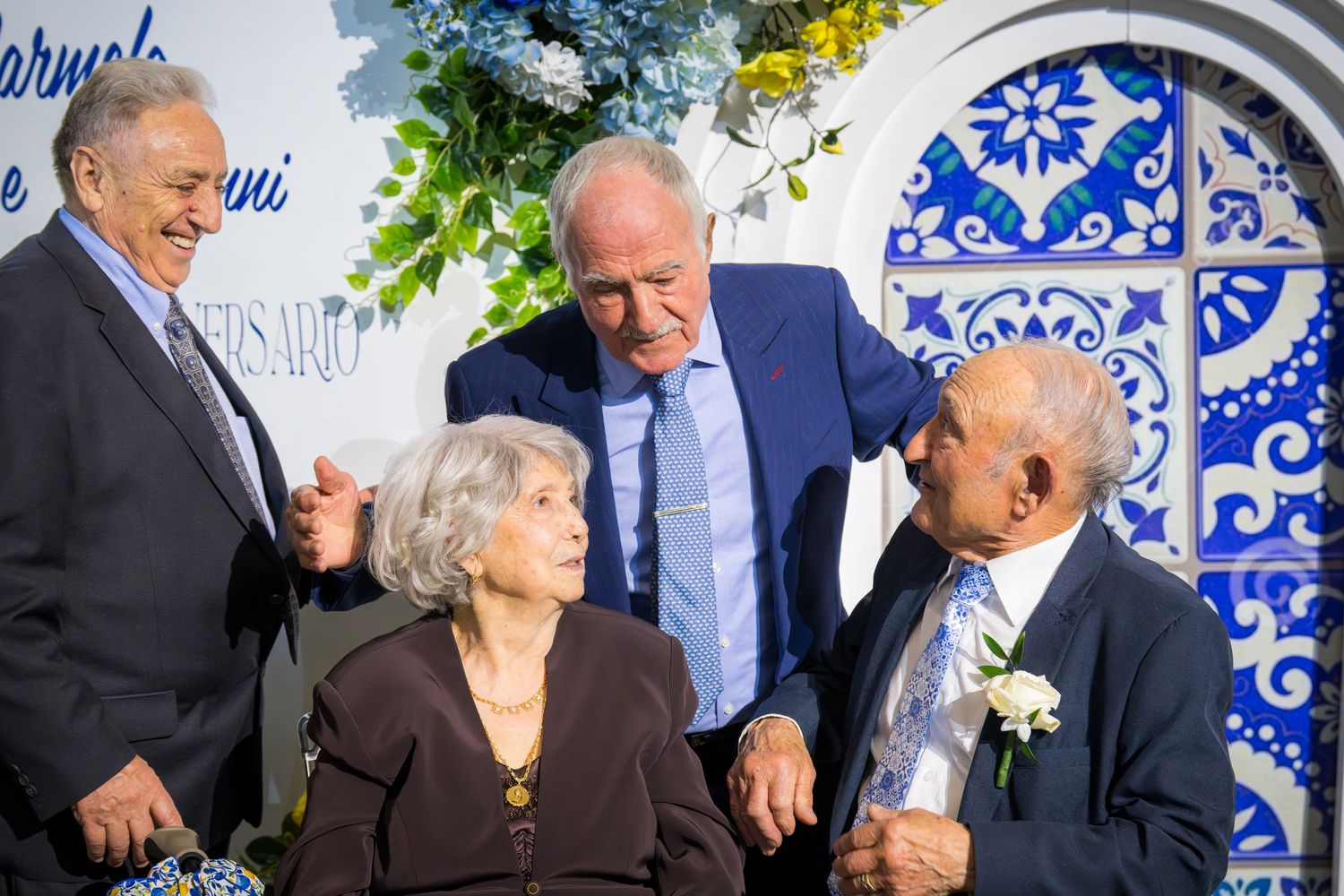 Group of four elderly people conversing and smiling at an anniversary celebration outdoors.