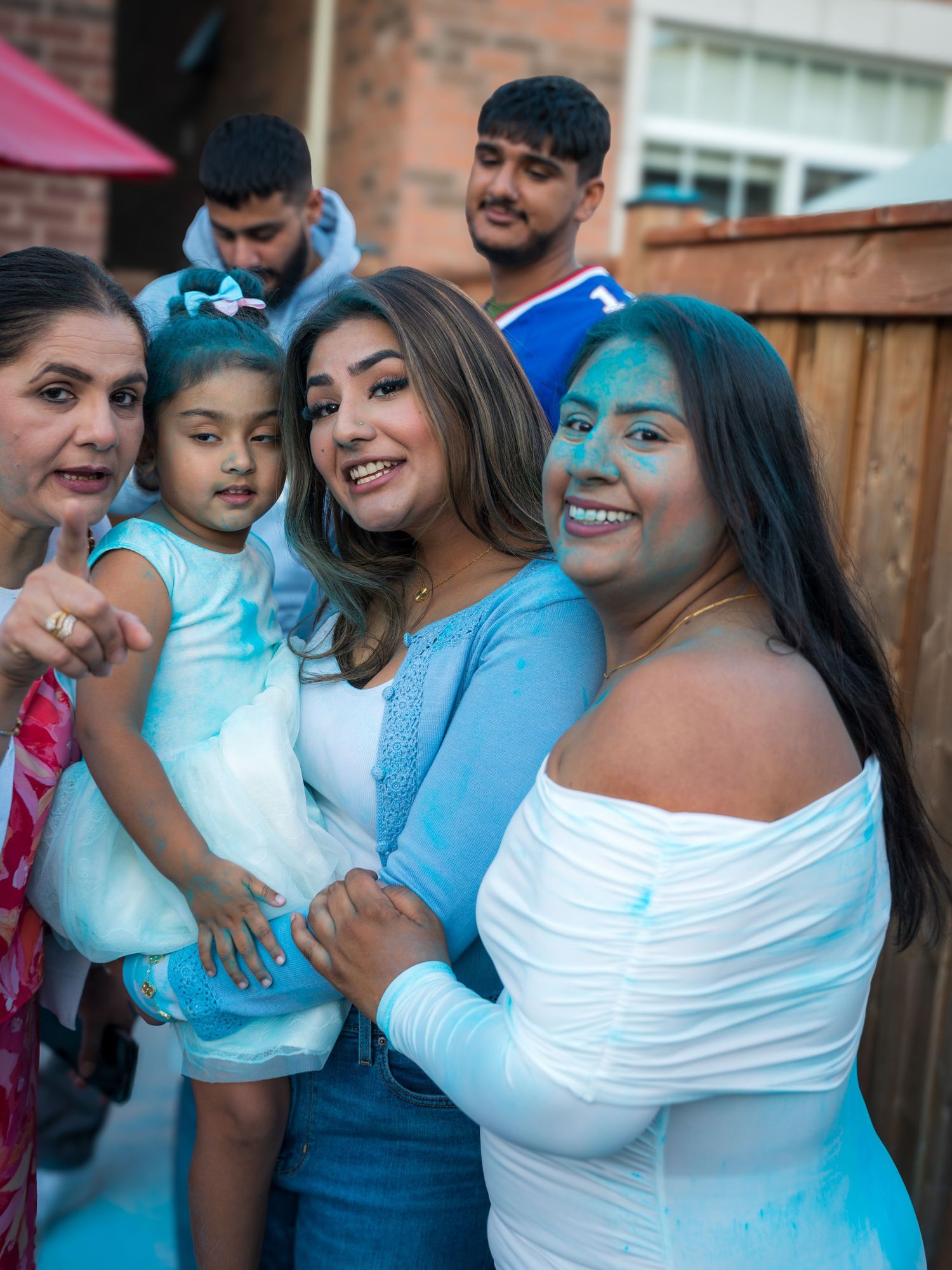 Women celebrating a gender reveal party covered in blue powder with a young child nearby.