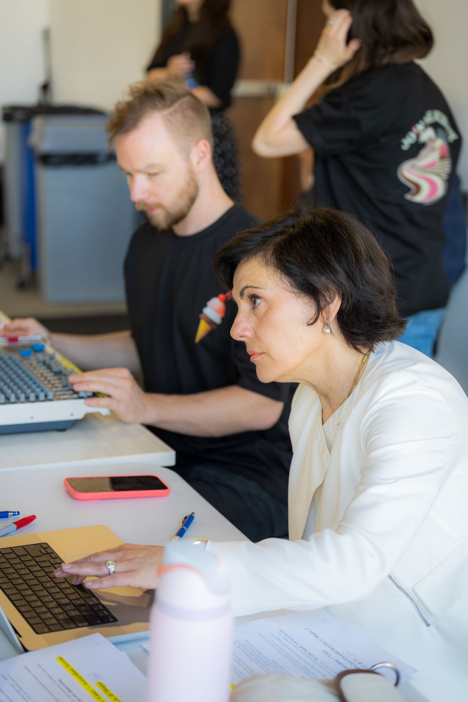 Man and woman working on laptops at sound mixing table during live event production.