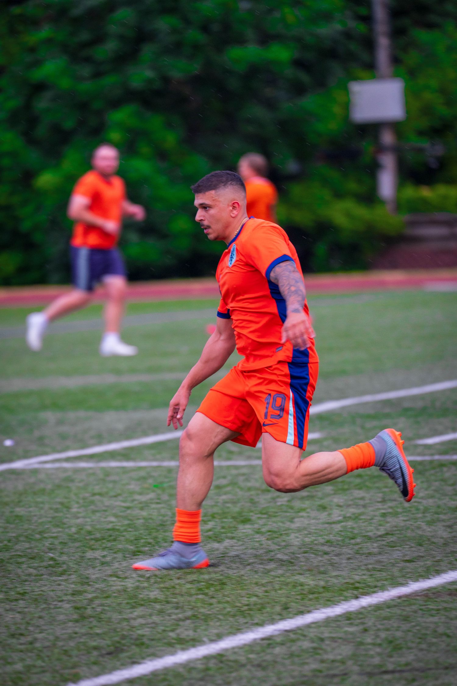 Player in orange jersey demonstrating dynamic stretching exercises on soccer field.