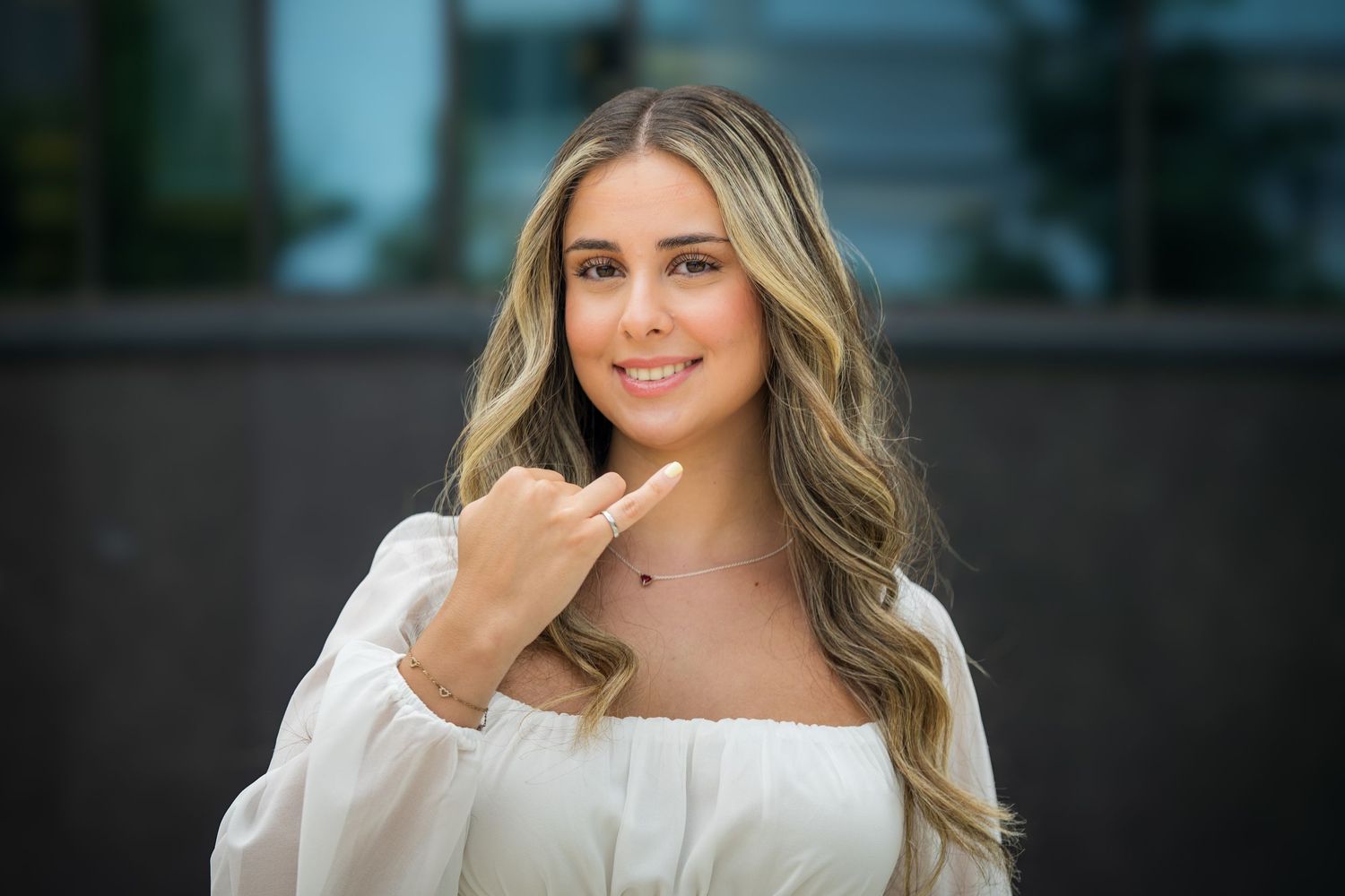Graduate with styled blonde waves poses in white dress for professional portrait.