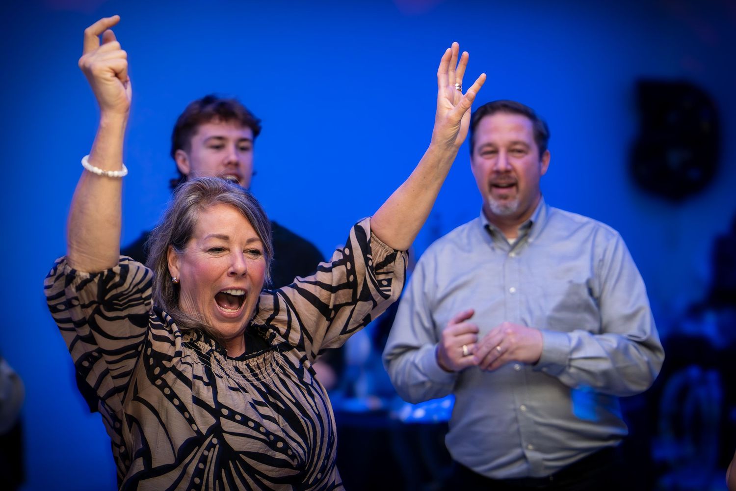 Enthusiastic dancers celebrating with arms raised against blue backdrop at indoor event.