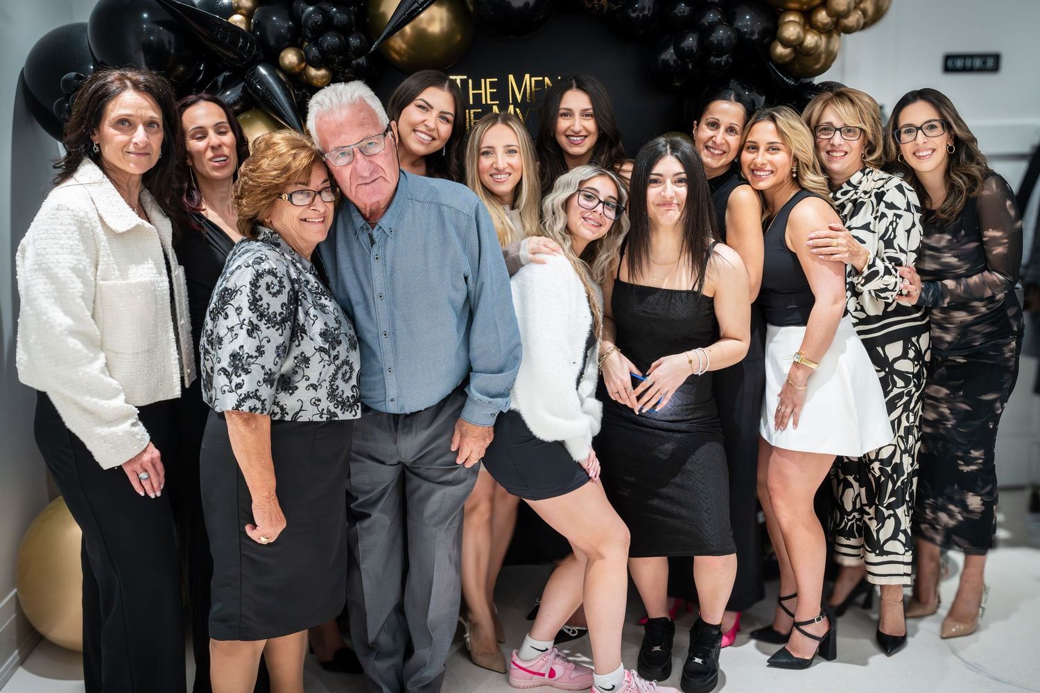 Social gathering with guests posing in front of black and gold party backdrop.