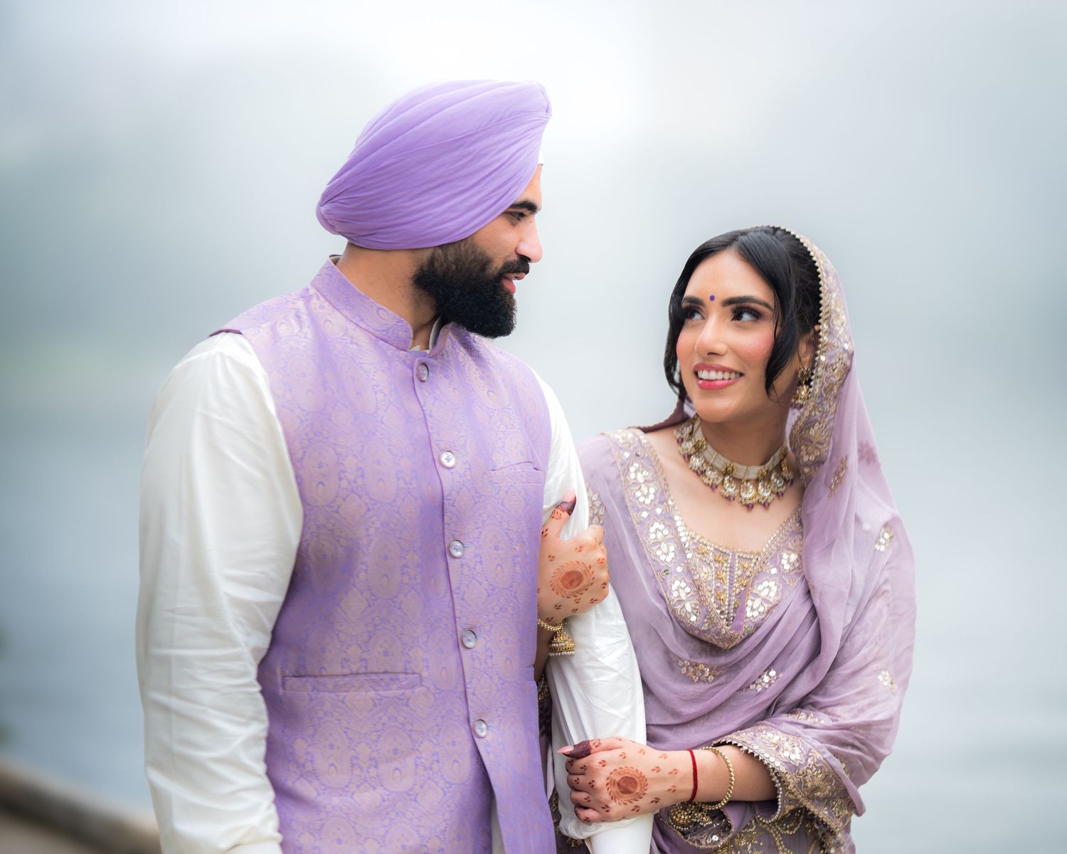 Romantic couple in coordinated purple outfits pose against a misty background.