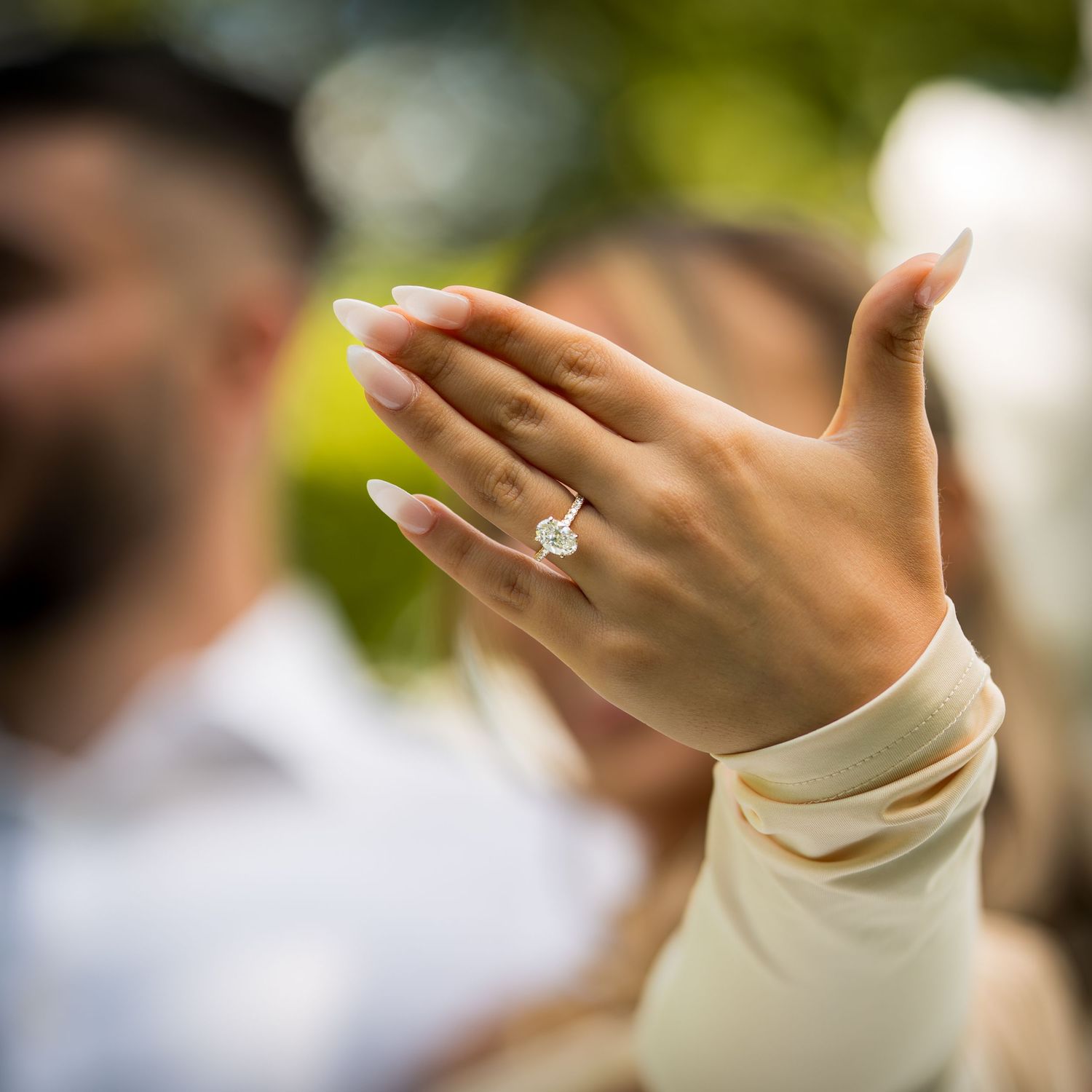 Detailed view of diamond engagement ring on hand with ivory sleeve in natural lighting.
