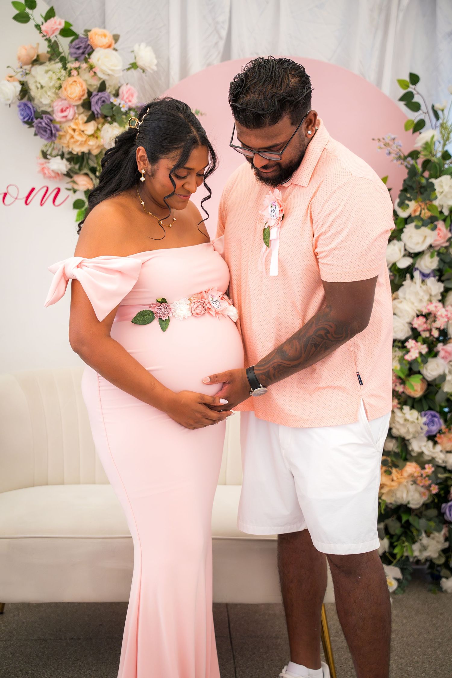 Baby shower photoshoot with couple in matching pink and white outfits.