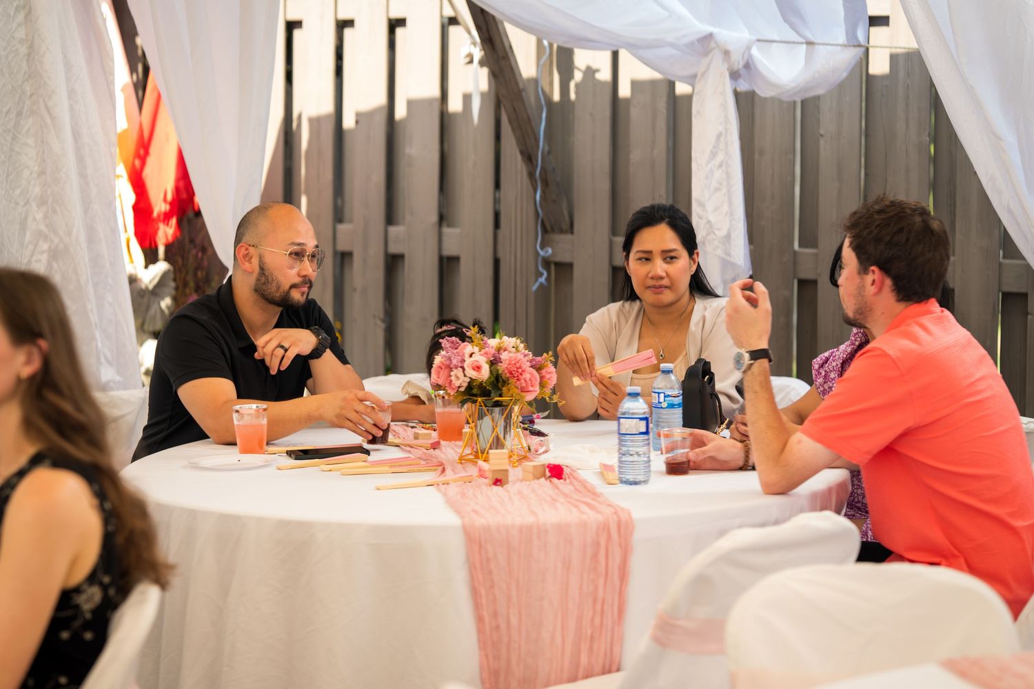 Group gathered at tables decorated with pink linens and white draping for a celebration.