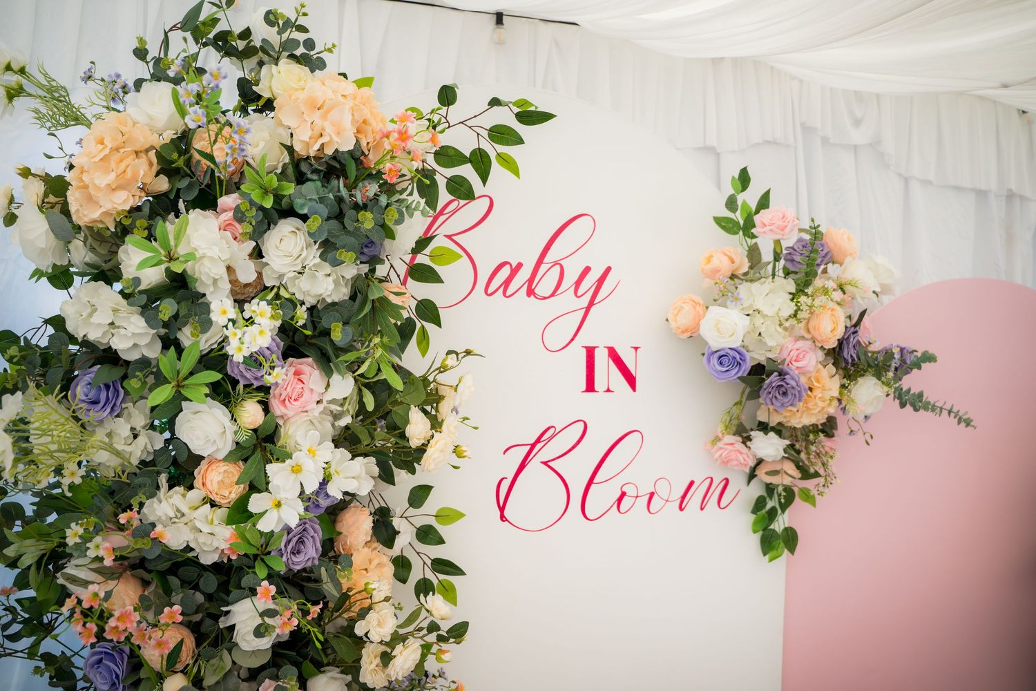 Baby shower backdrop with 'Baby Bloom' text surrounded by elegant floral arrangements.