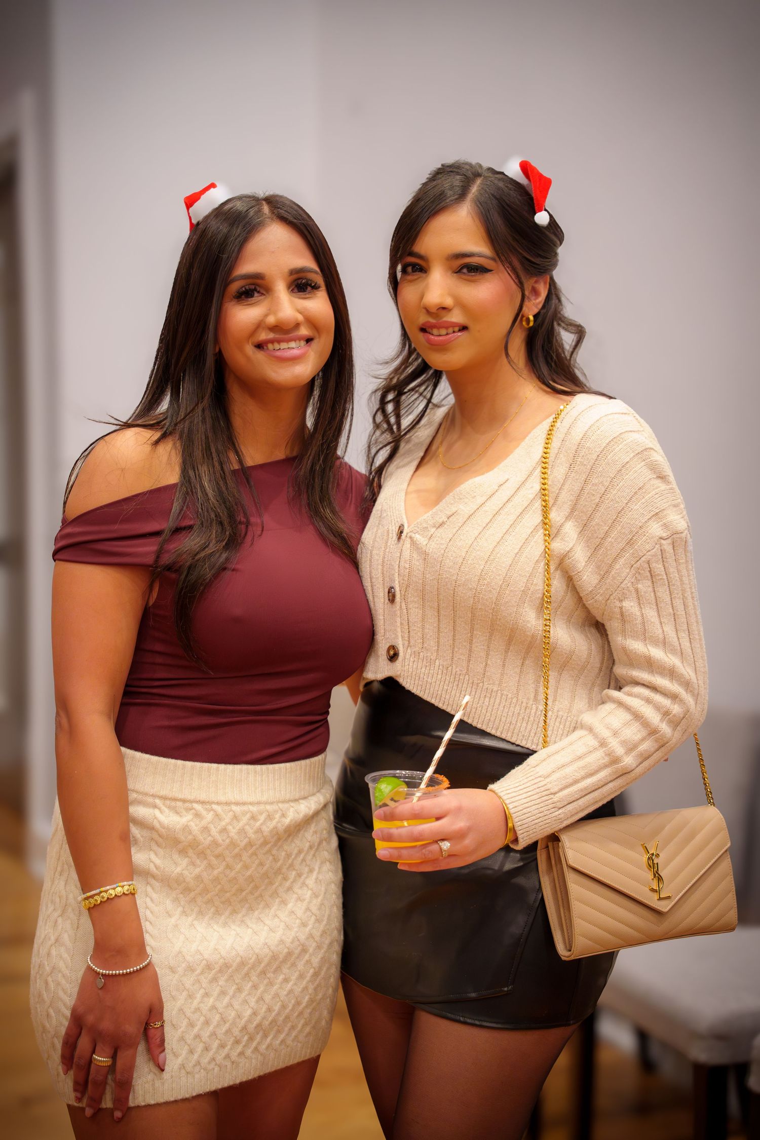 Two friends pose together at a social gathering, one wearing burgundy and one in a cream cable knit sweater.