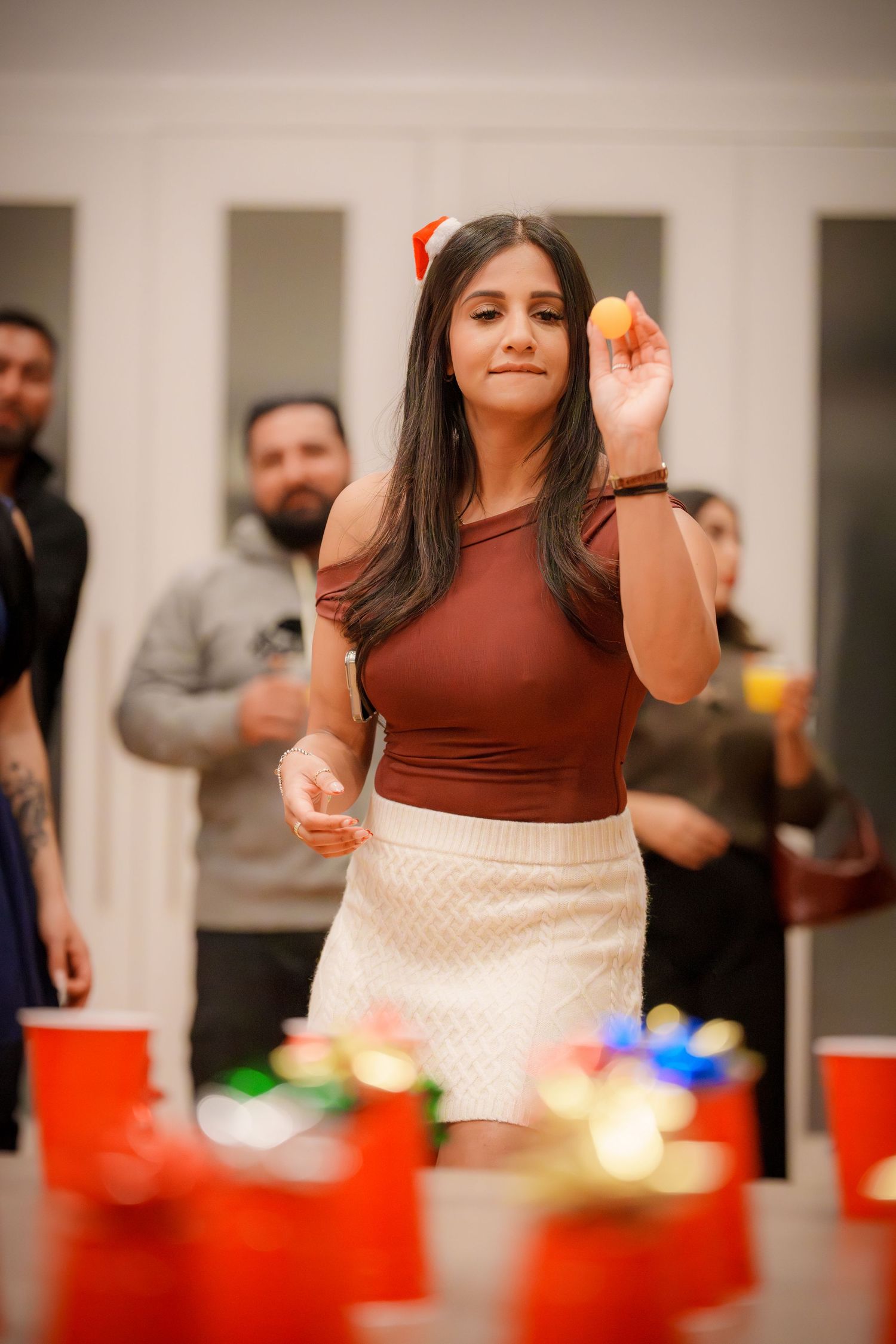 Person in brown top and white skirt smiles while gesturing at holiday party.