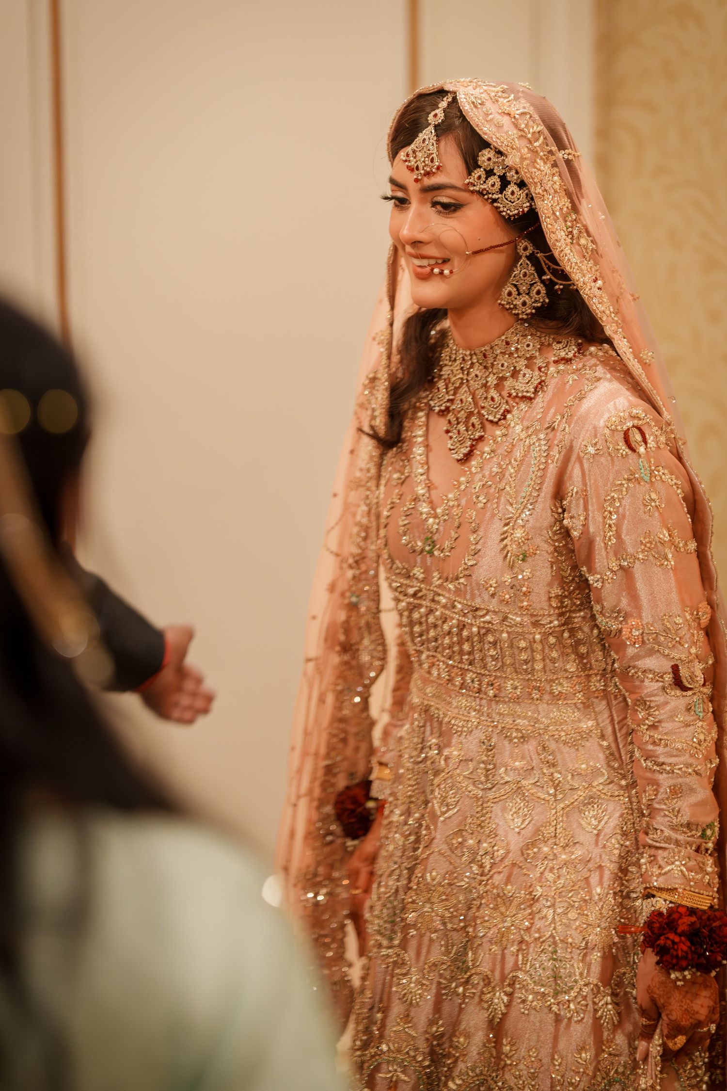 Candid moment of bride in blush pink embellished lehenga smiling during wedding celebration.