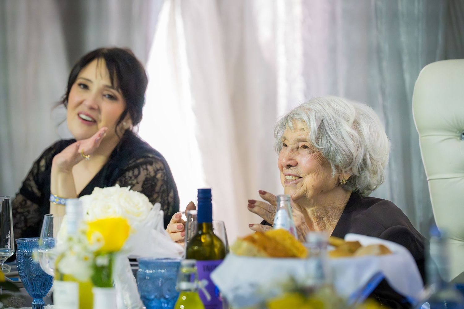 Two women laughing and enjoying conversation at an anniversary celebration dinner with yellow floral decor.
