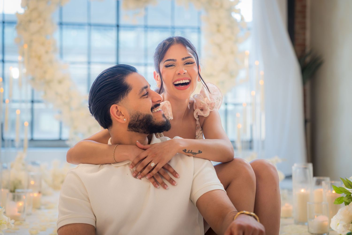 Joyful couple embracing and laughing together surrounded by white floral arrangements and candles.