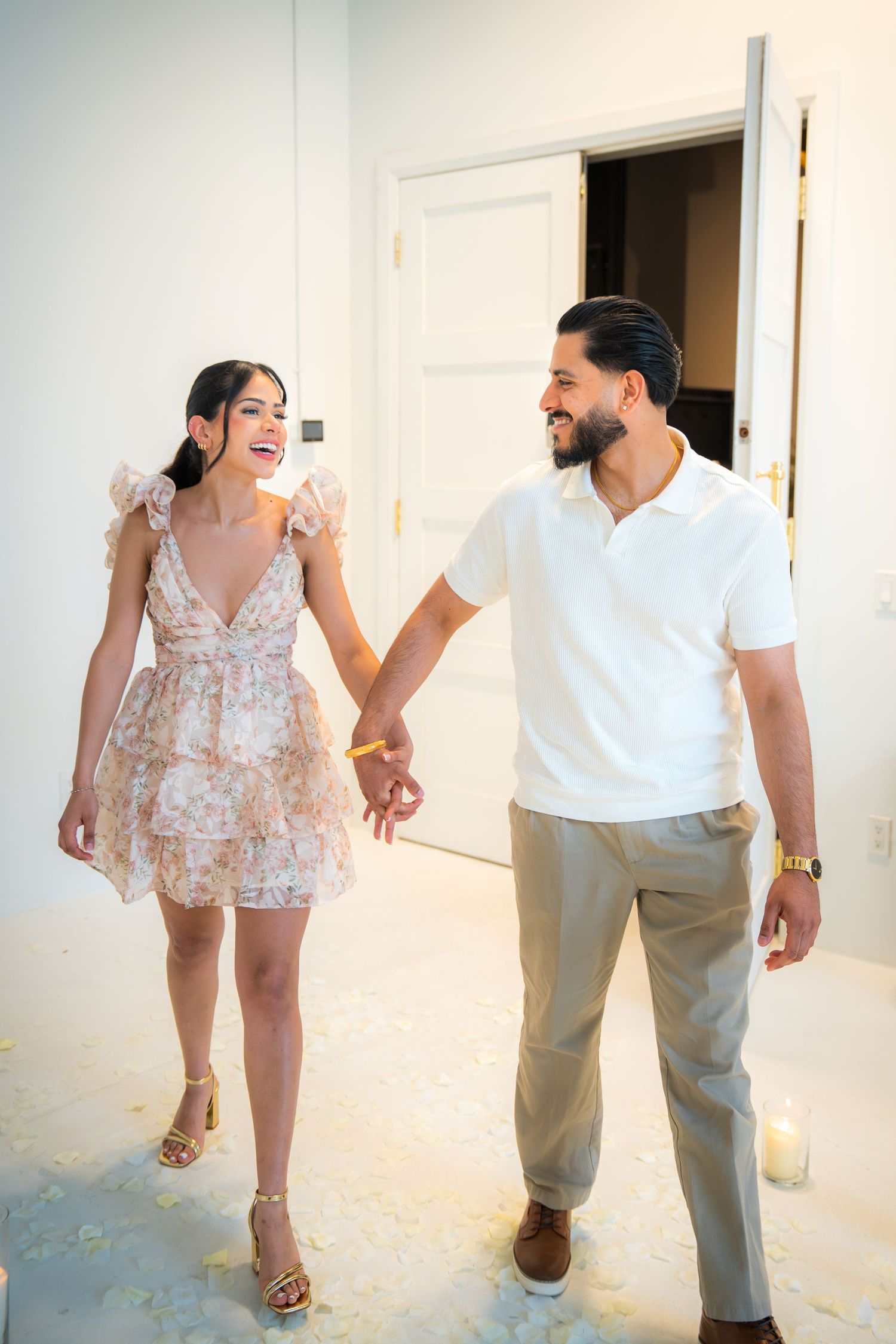 Smiling couple holding hands walking together, woman in floral mini dress and man in white polo shirt.