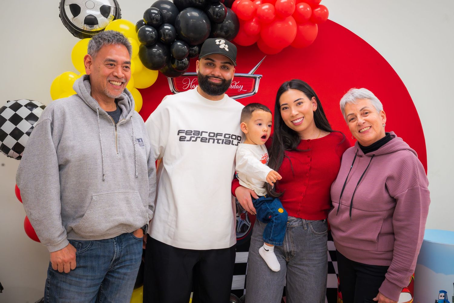 Family of five posing together at a Cars themed birthday party with balloon decorations in the background.