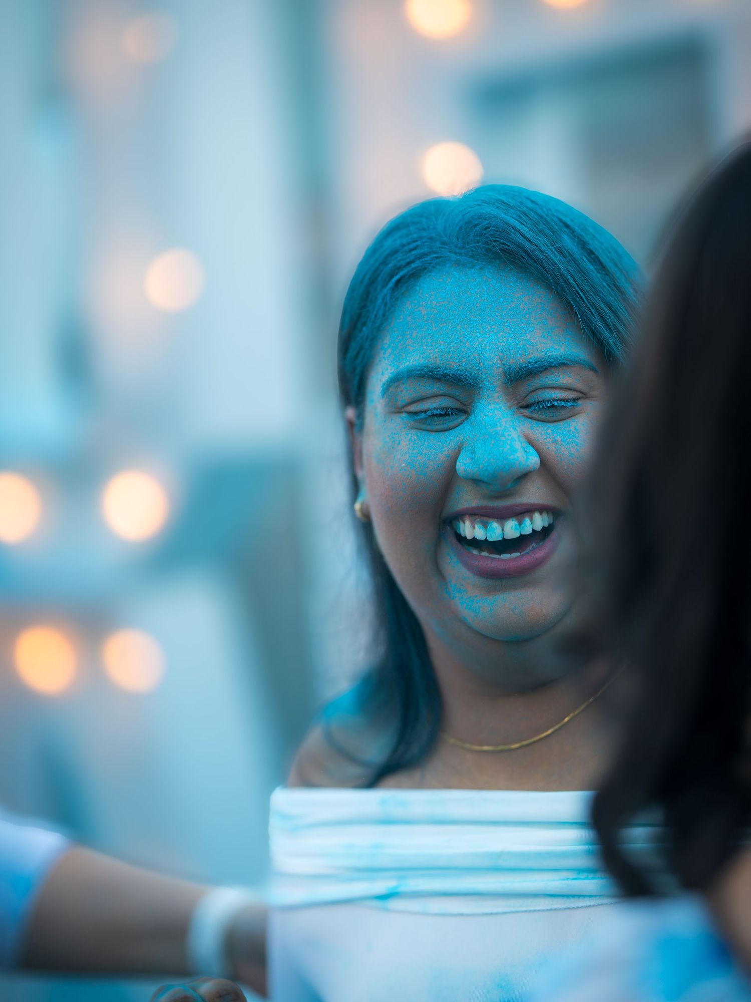 Woman laughing joyfully with blue Holi powder on her face at a festive celebration.