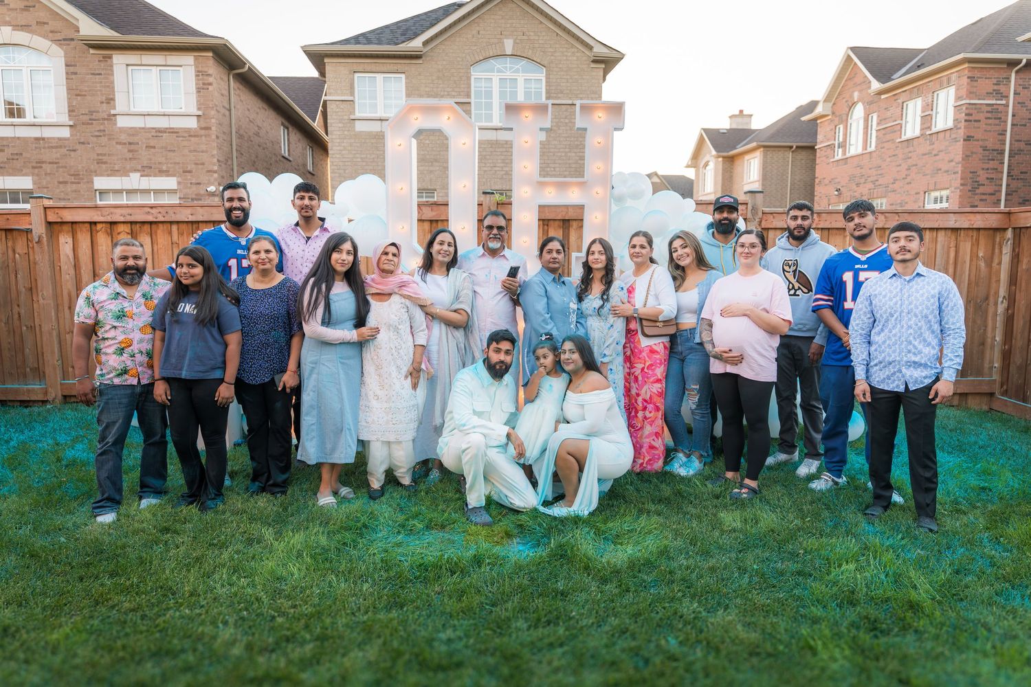 Large group photo at gender reveal party with OH BABY sign and white balloons in backyard.