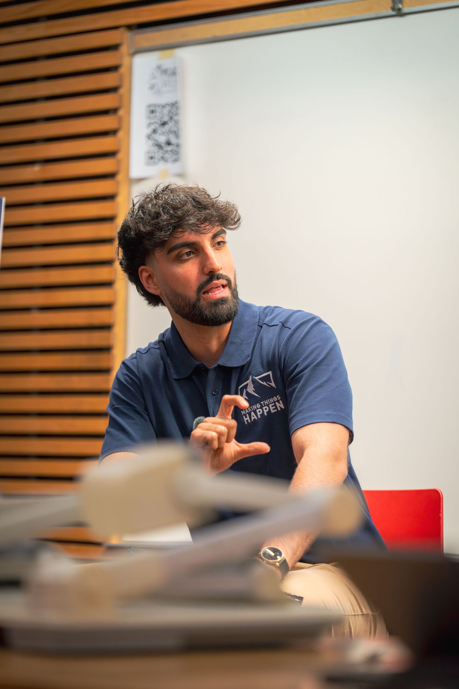 Speaker in a navy polo shirt gesturing during a presentation in a classroom.