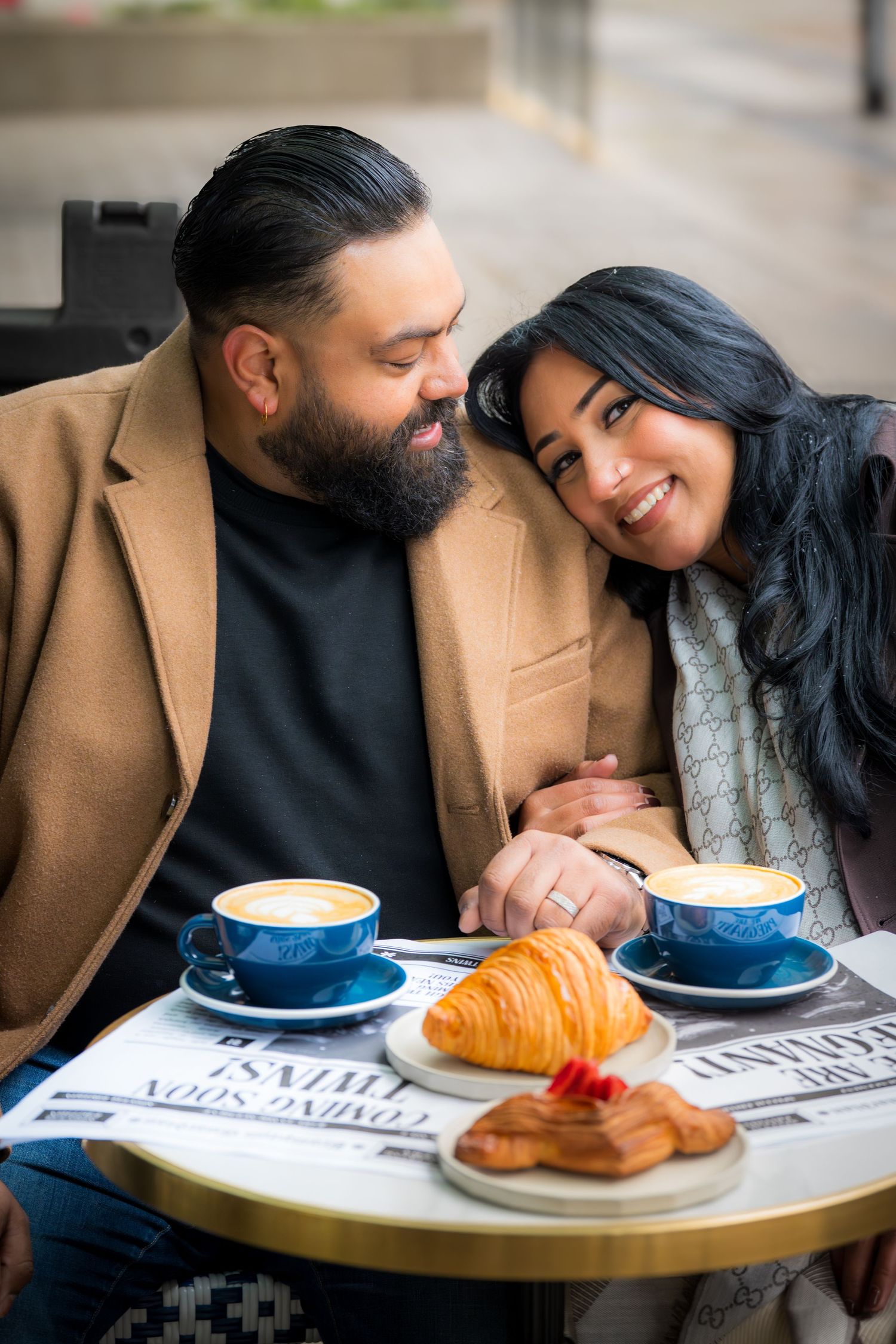A couple shares an intimate moment at a cafe table with coffee and croissants.