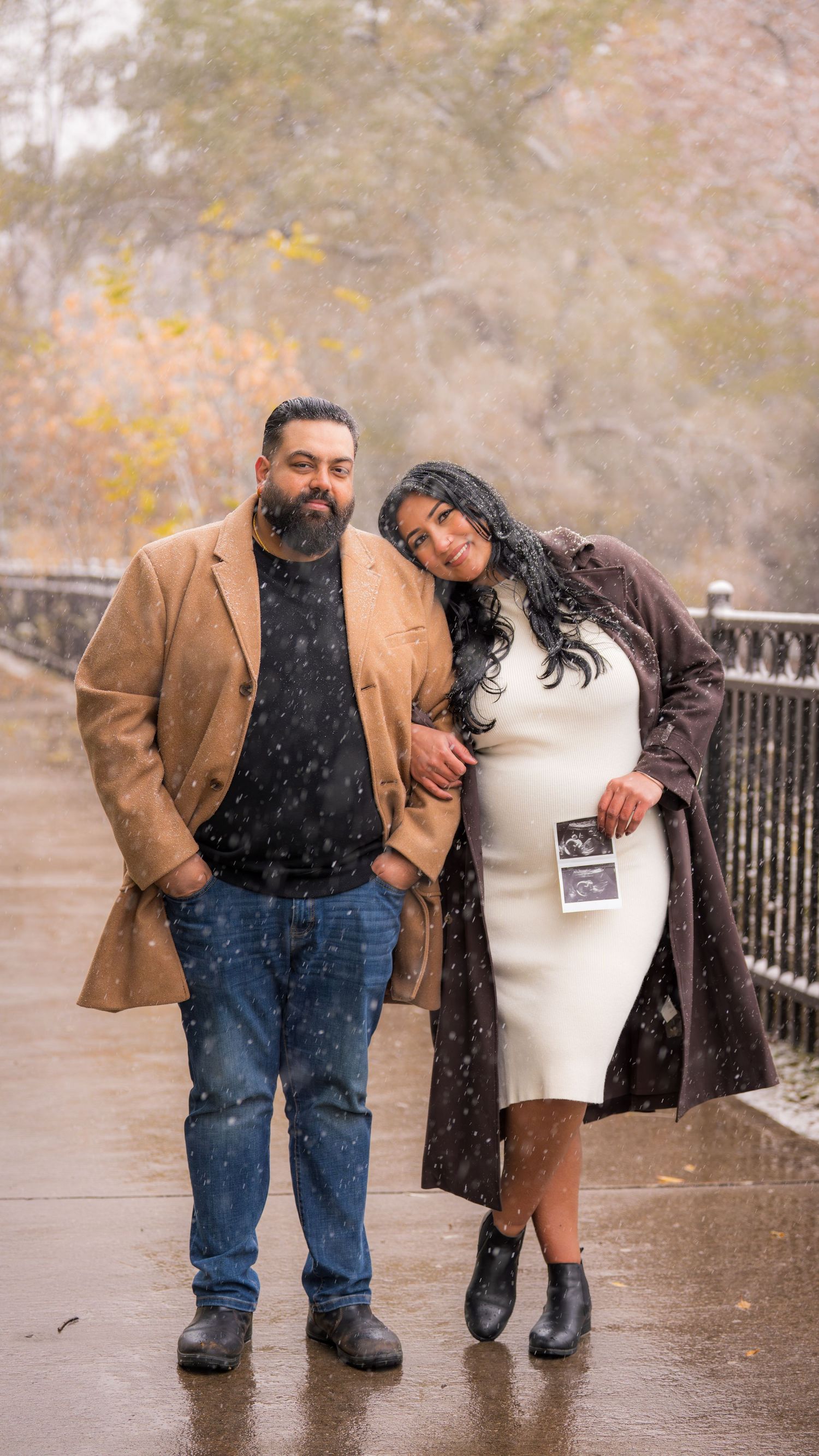Romantic couple posing in the snow while holding an ultrasound photo.
