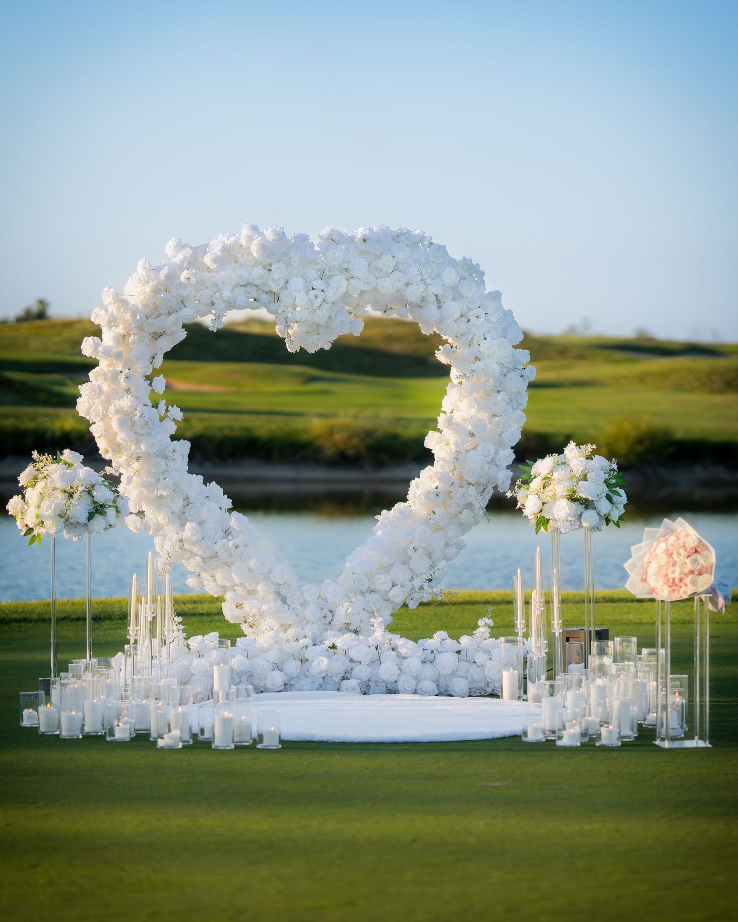 Elegant white floral arch setup for outdoor wedding ceremony by a lake.