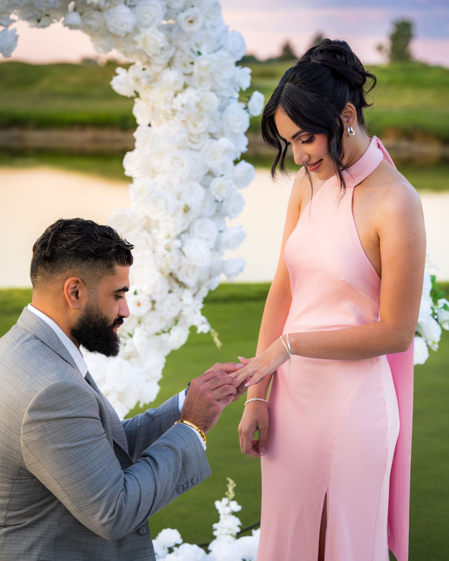 Surprise proposal moment under a white floral arch with romantic lighting.