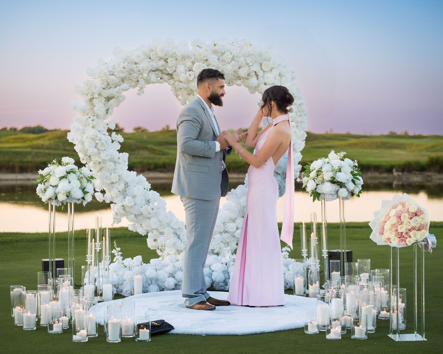 Romantic proposal scene with white floral decorations and lanterns at golden hour.