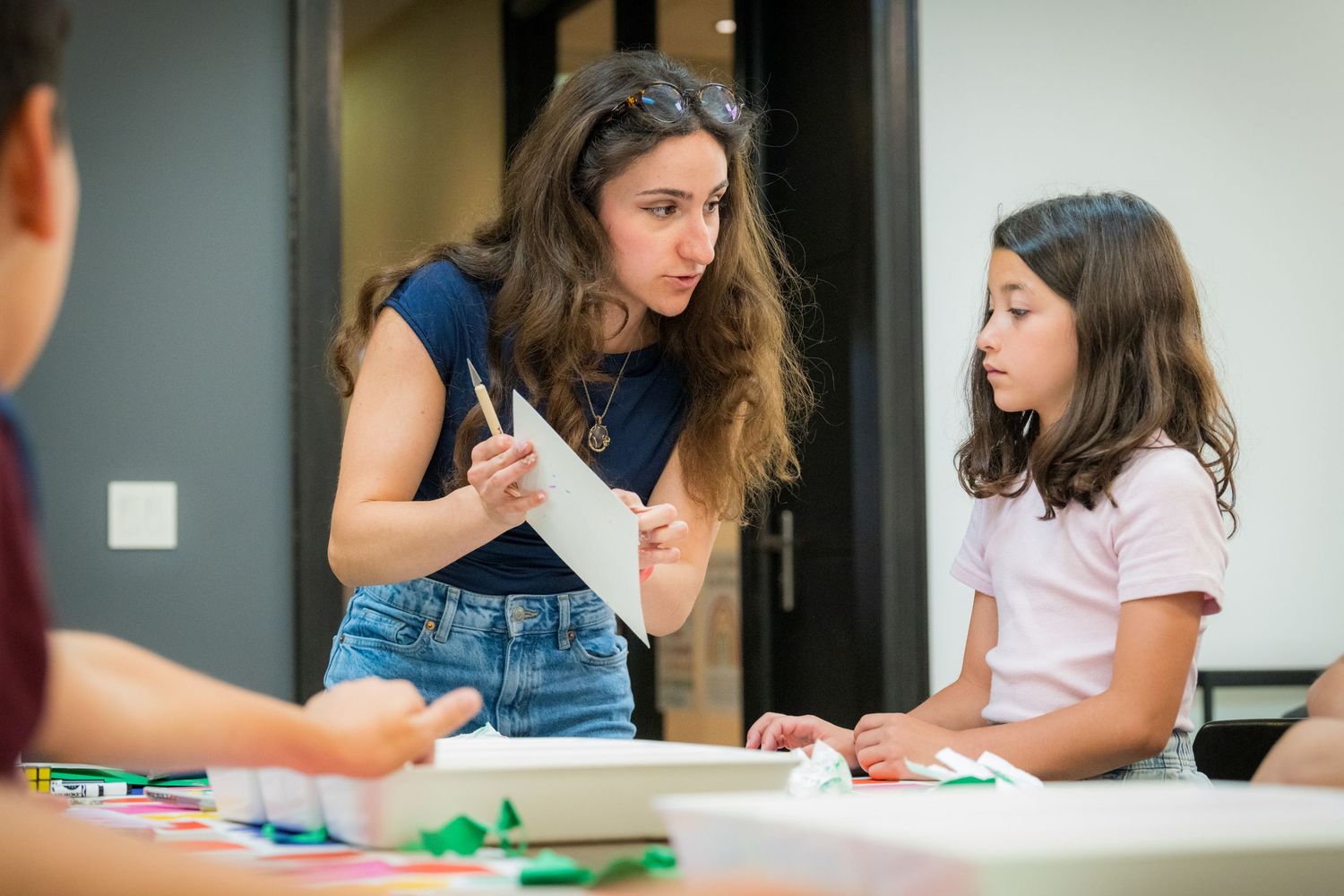 A female art teacher shows a young girl a drawing during a creative art workshop class.