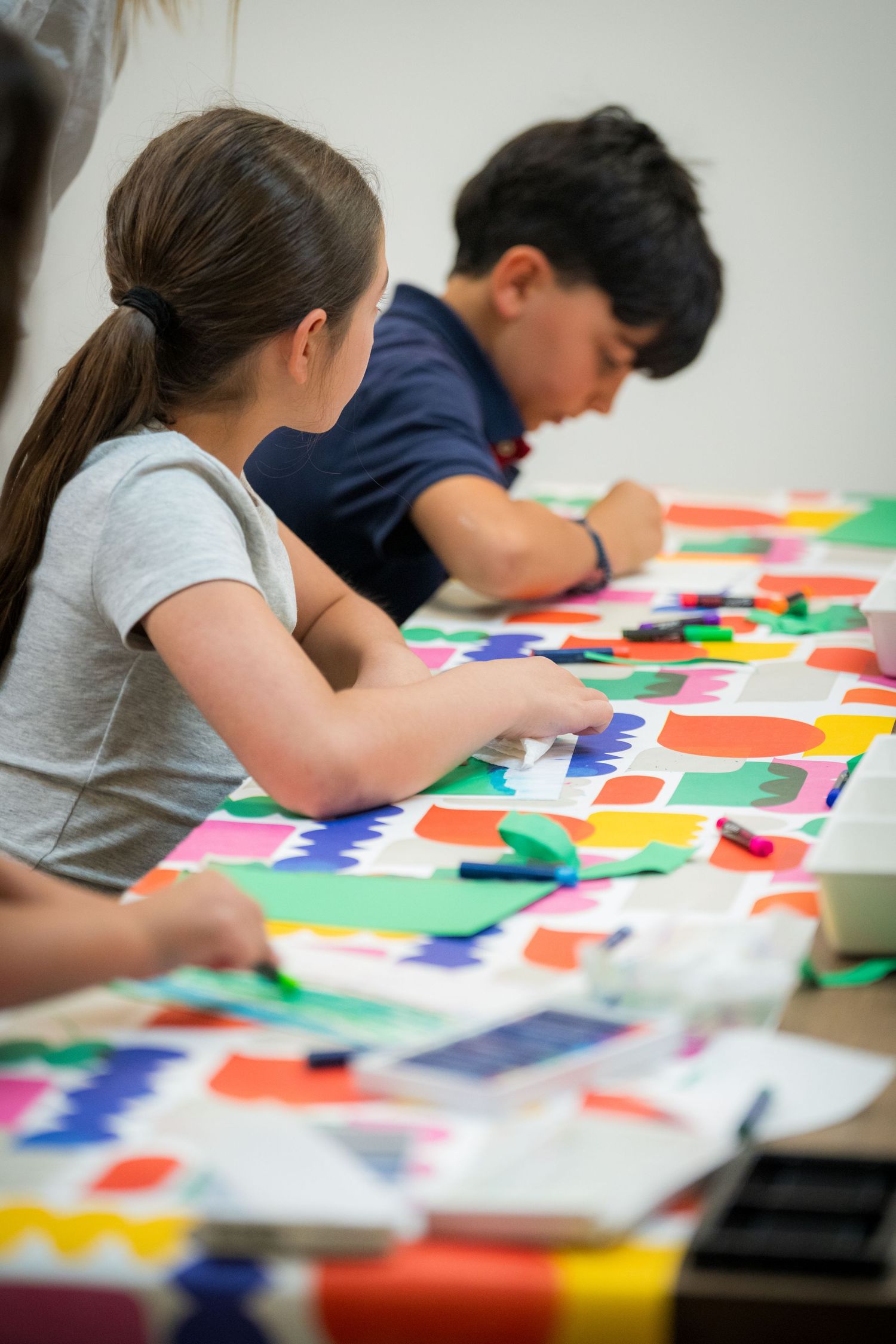Children engaged in colorful paper cutting art activity at a bright table during a creative workshop.