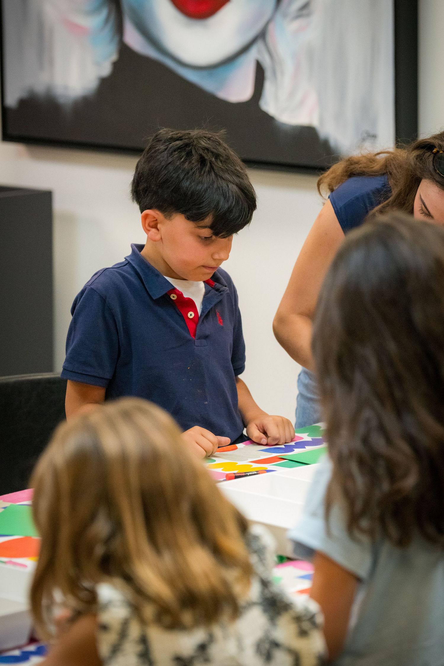 Young boy focuses on colorful paper craft activity at an art workshop table.