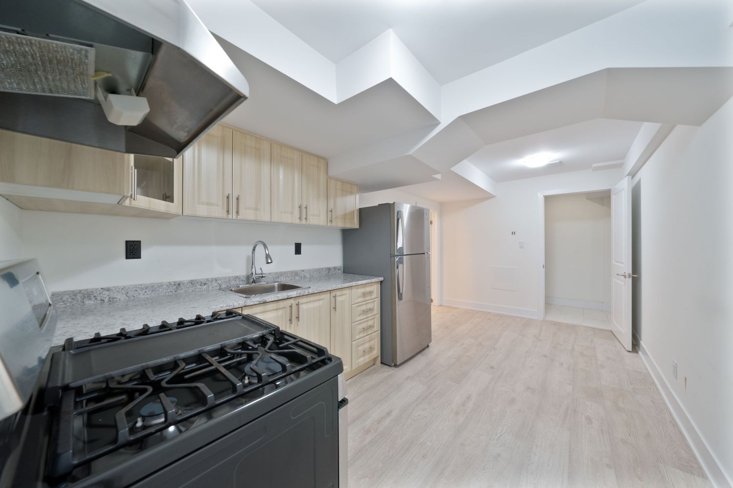 Modern apartment kitchen renovation showing light wood floors, white cabinets, and stainless steel appliances.