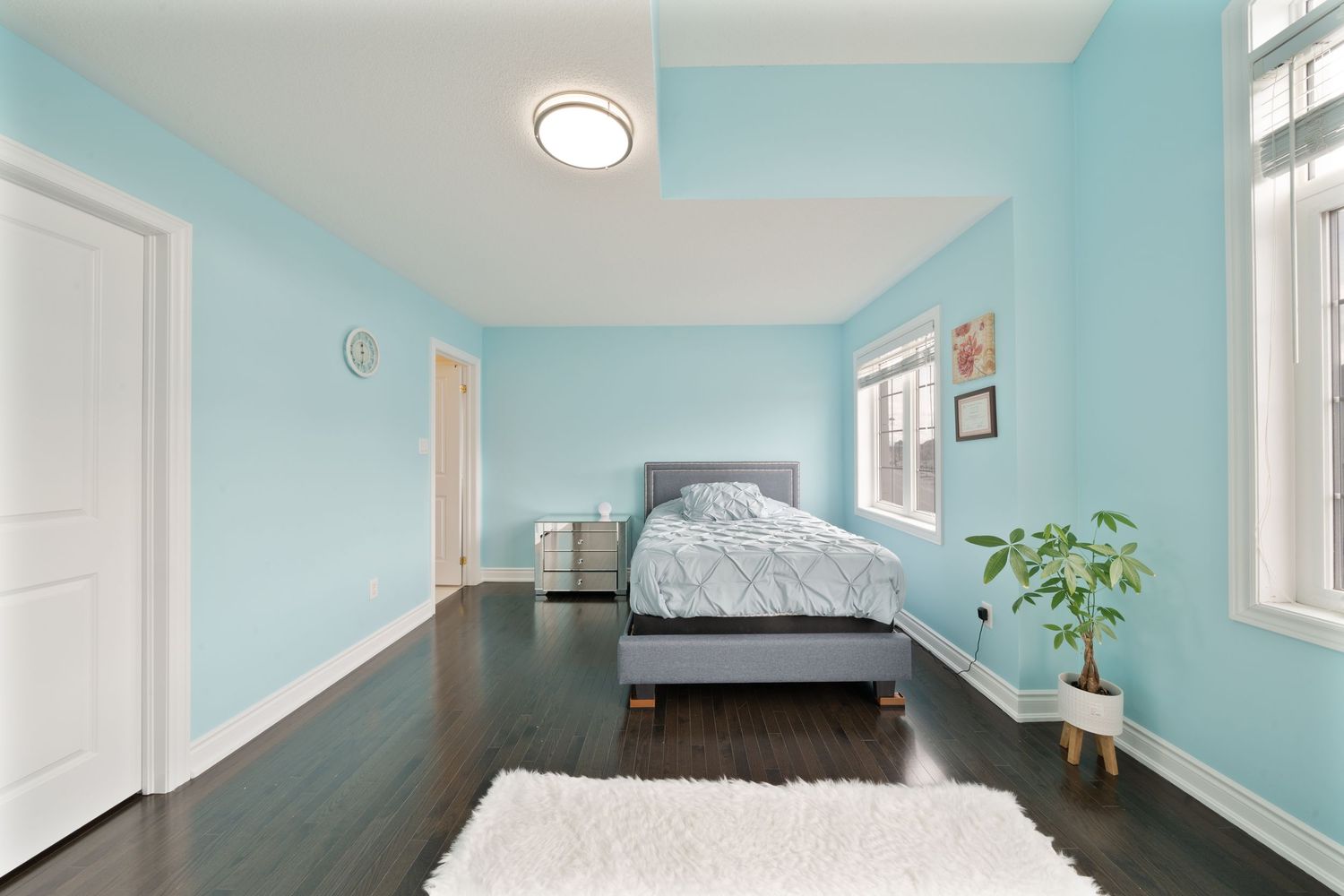 A bright and airy bedroom with light blue walls, white trim, and natural light streaming through multiple windows.