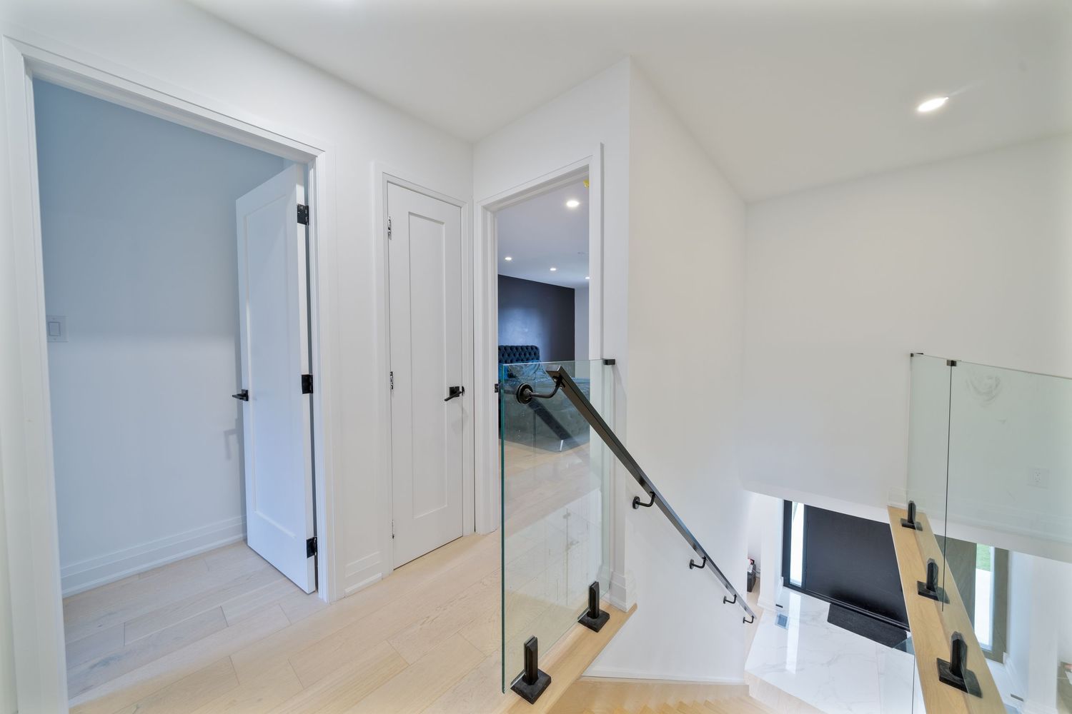Modern white interior hallway with hardwood flooring and recessed lighting showcases multiple doorways and clean lines.