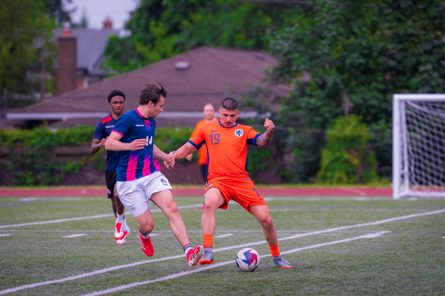 Soccer players in orange and blue uniforms practicing on field with goal visible in background.